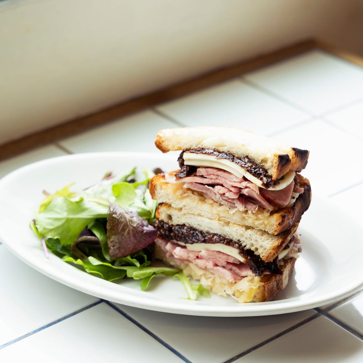 A sandwich featuring homemade low-temperature cooked roast ham with prune jam. The balance of saltiness, umami, and fruitiness is accented by the tang of sauerkraut.