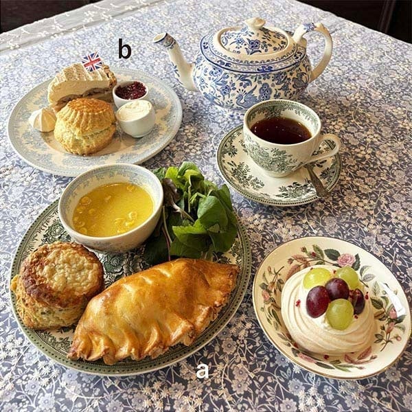 Enjoy a variety of afternoon tea sets and desserts, including the Afternoon Tea Reservation Royal Orange Afternoon Tea Set for ¥9,900 (tax included), Blue Moon Savory Lunch Plate for ¥3,850, and Scone & Cake Plate for ¥2,750. Limited-time offerings include the Bake Shop Rotary Cake Plate for ¥3,300 and Savory Plate for ¥3,780. Refreshing drinks such as the Land of the Bitter Orange Tea at ¥990 and Lemon Curd Eton Mess Parfait at ¥990 are also available. Scones range from ¥411 to ¥508, and specialty fudge is ¥1,296 per 100g. Other items include Welsh Cakes at ¥491 each, Fish & Chips at ¥2,178, and exclusive collectible mugs and scarves priced from ¥20,900 to ¥74,800.