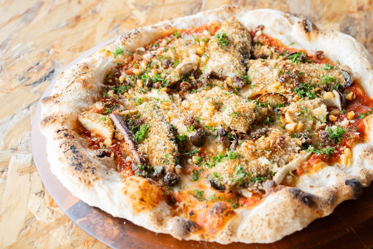 A seasonal pizza topped with grilled sanma and earthy mushrooms, enhanced with herbs and without cheese, offering a delightful taste at ¥1,800 (tax included).