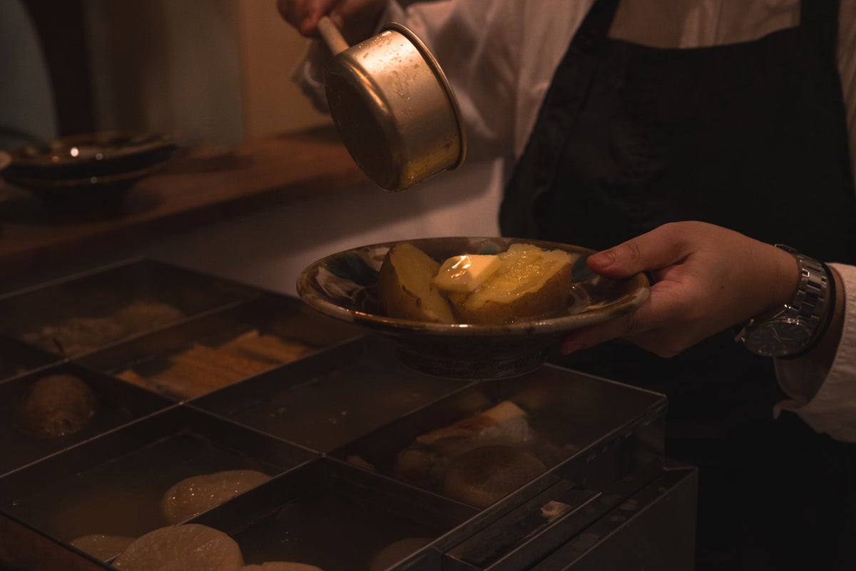 A corner-style oden pot in front of the counter. It features daikon simmered in shellfish broth, homemade fish paste with sardines and coriander, octopus, and more.