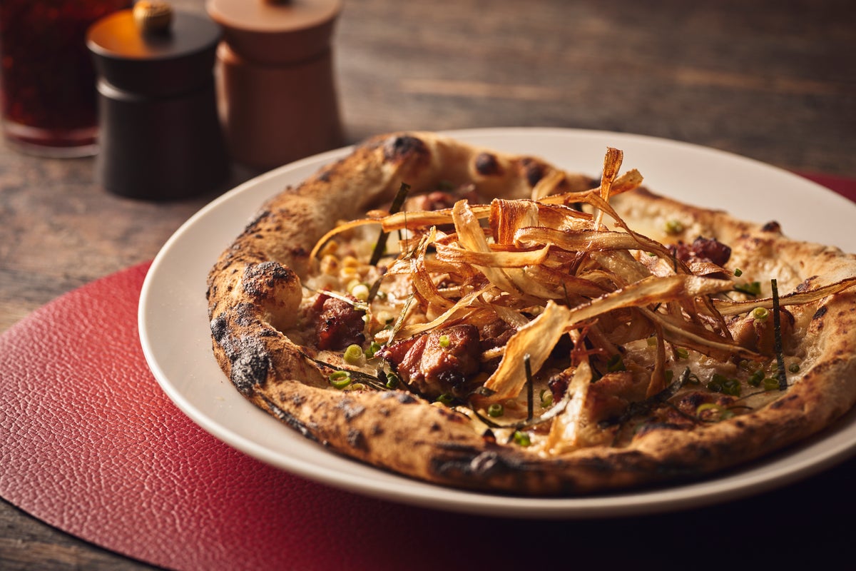 The pizza with grilled chicken, corn, nori, and burdock combines Italian pizza craftsmanship with Japanese ingredients. Topped with tender grilled chicken, sweet corn, fragrant nori, and burdock, finished with a special sweet sauce passed down for 52 years. It offers a familiar, savory flavor with the umami of chicken and sauce, and the aroma of nori and burdock. It can be enjoyed with prosciutto upon request.