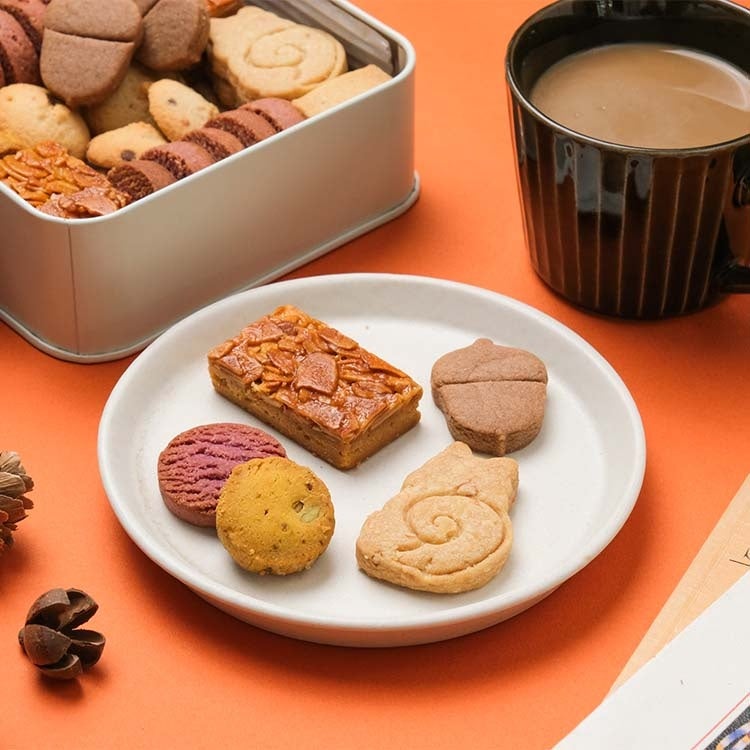 When thinking about creating an autumn cookie tin, squirrels and acorns immediately come to mind. The result is a delightful cookie tin with adorable squirrel and acorn motifs. It includes cookies made with nuts, pumpkin, and purple sweet potato, along with familiar chocolate chip cookies and vanilla shortbread. The textures range from crispy and crumbly to crunchy and firm, offering a variety of textures to enjoy during a peaceful autumn snack break. The goal is to bring a cozy autumn atmosphere to your day.