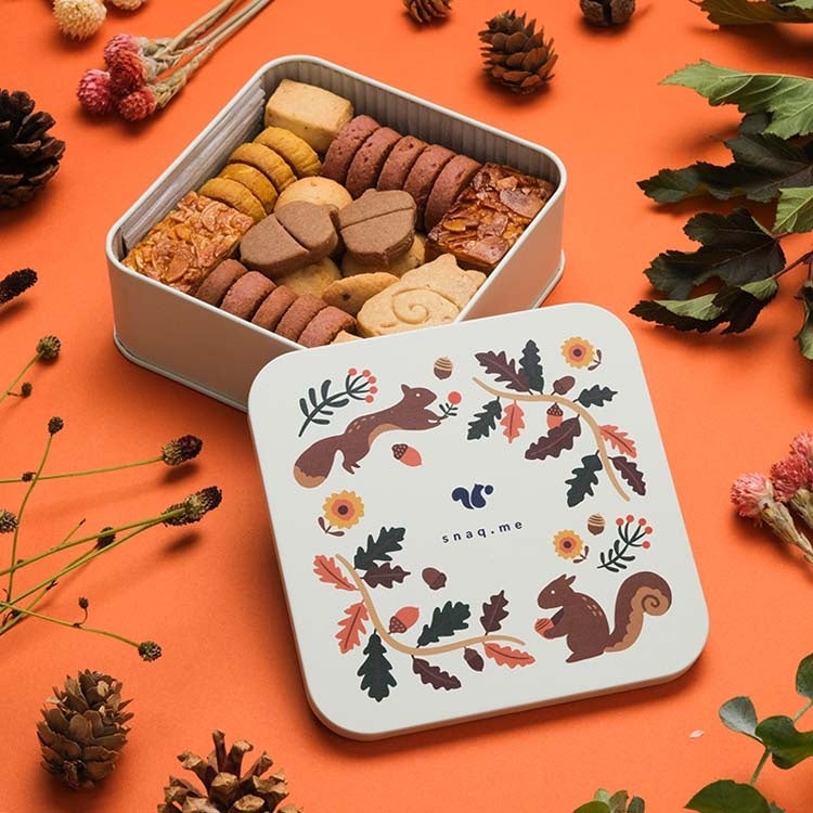 This cookie tin is designed to evoke a squirrel searching for acorns in an autumn-colored forest. The design is inspired by the cookies inside, featuring motifs of colorful leaves, nuts, and autumn flowers, depicting a scenic autumn forest. It aims to capture the essence of fall in a charming and artistic way.