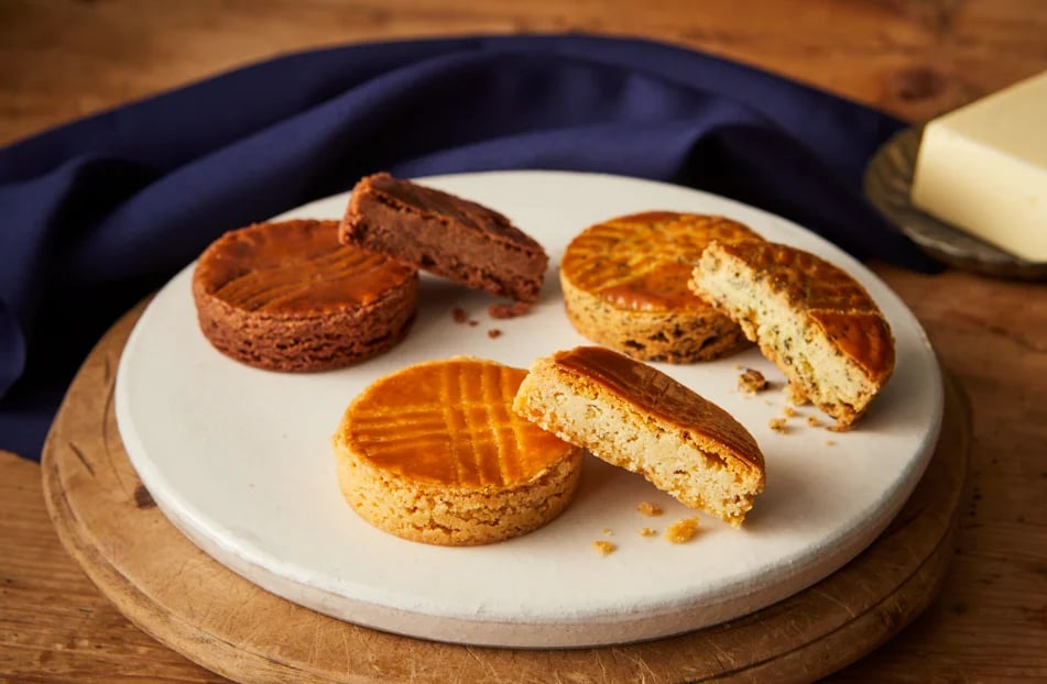 Palet Breton, a traditional baked good from Brittany, France. It features a sun motif and has a crispy, thick cookie with a buttery flavor. Available in three varieties: Plain, Chocolate, and Earl Grey.