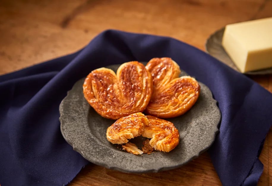 Palmier, a flaky pastry with multiple layers that crumbles easily. Caramelized sugar on the surface adds a toasty flavor. Known for its rich butter taste and light, fragrant caramel, this is a traditional French confection.